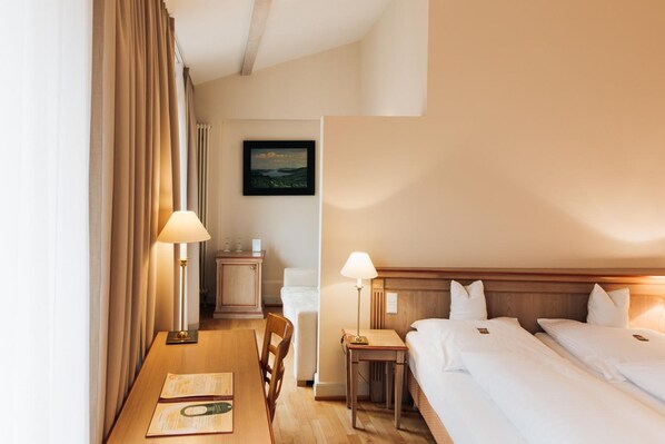 A hotel room with two beds, a desk, a chair, a nightstand, and a painting on the wall.