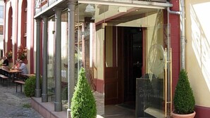 A building with a covered entrance, potted plants, and a seating area outside. - Kulturbrauerei Heidelberg AG (Heidelberg)