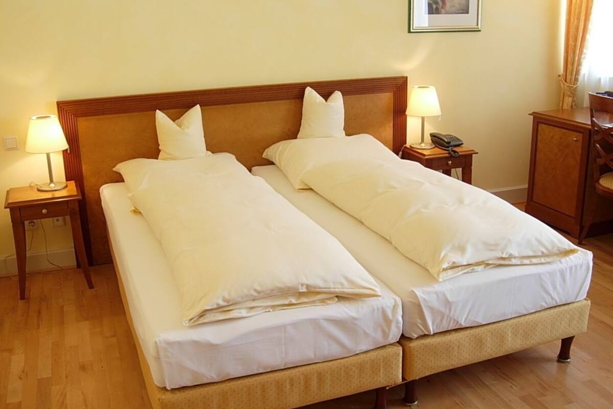 A double bed with two pillows, a wooden headboard, bedside tables with lamps, and a small cabinet.