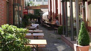 An outdoor café area with tables and chairs, surrounded by buildings with red brick and white facades. - Kulturbrauerei Heidelberg AG (Heidelberg)