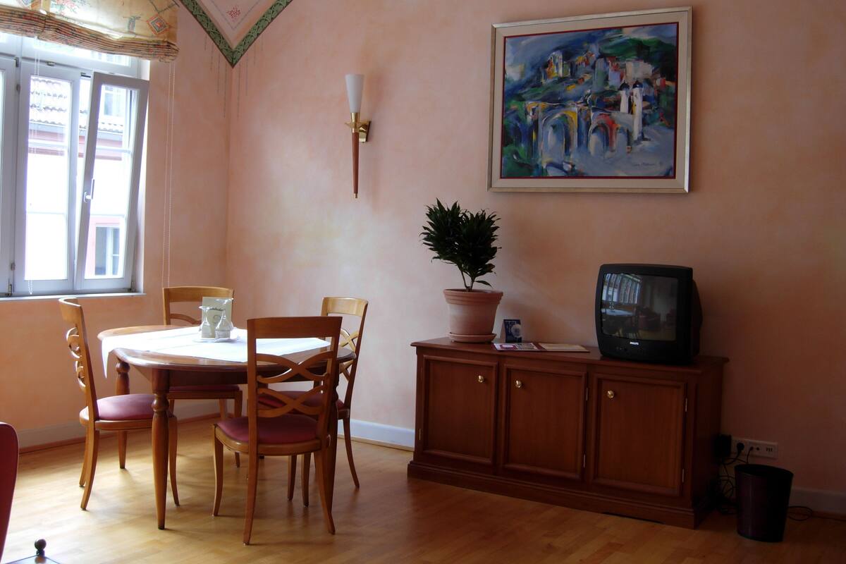 A dining area with a table, chairs, a potted plant, a television, and a cabinet.