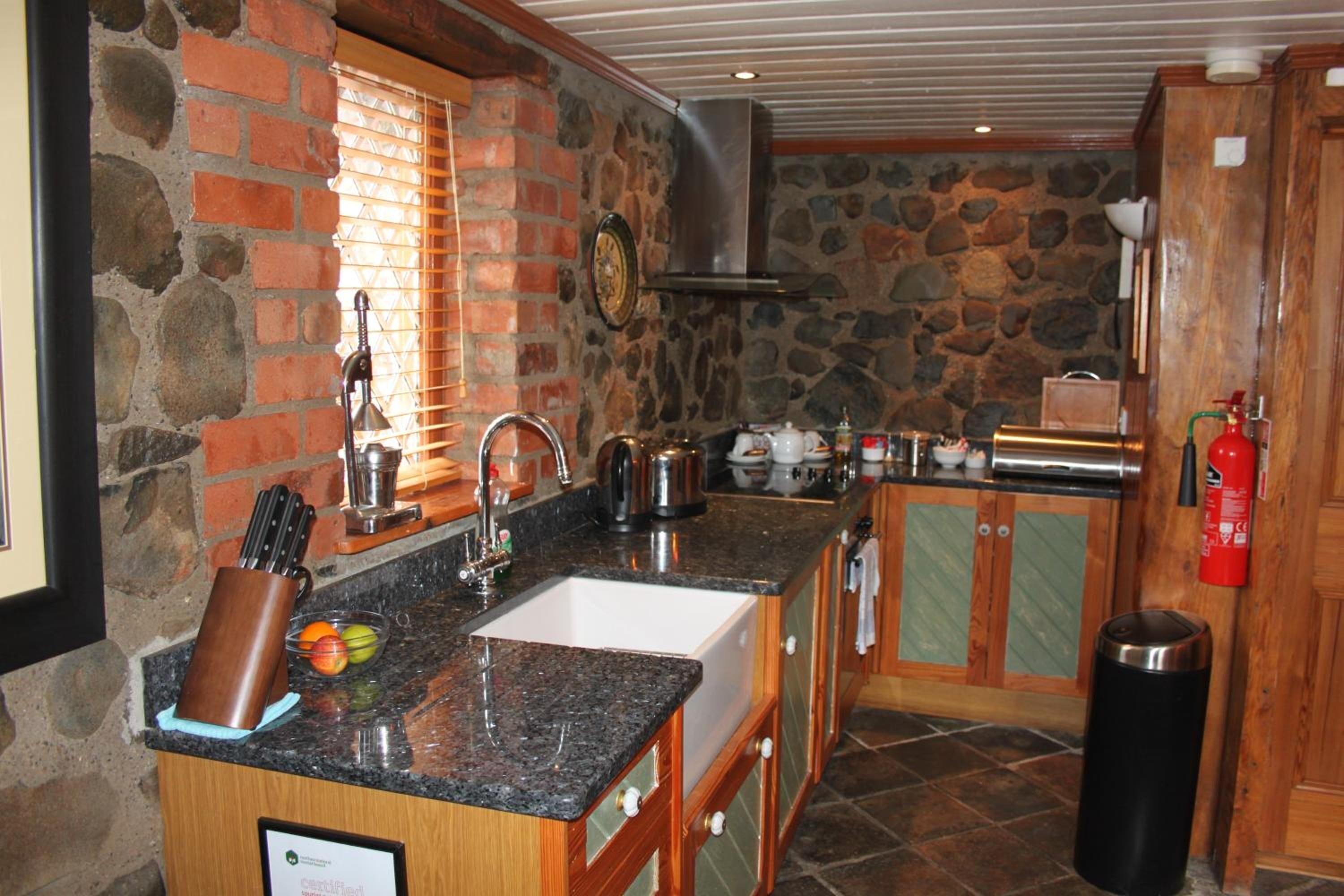 Una cocina con pared de piedra, un lavamanos y una ventana con persianas.