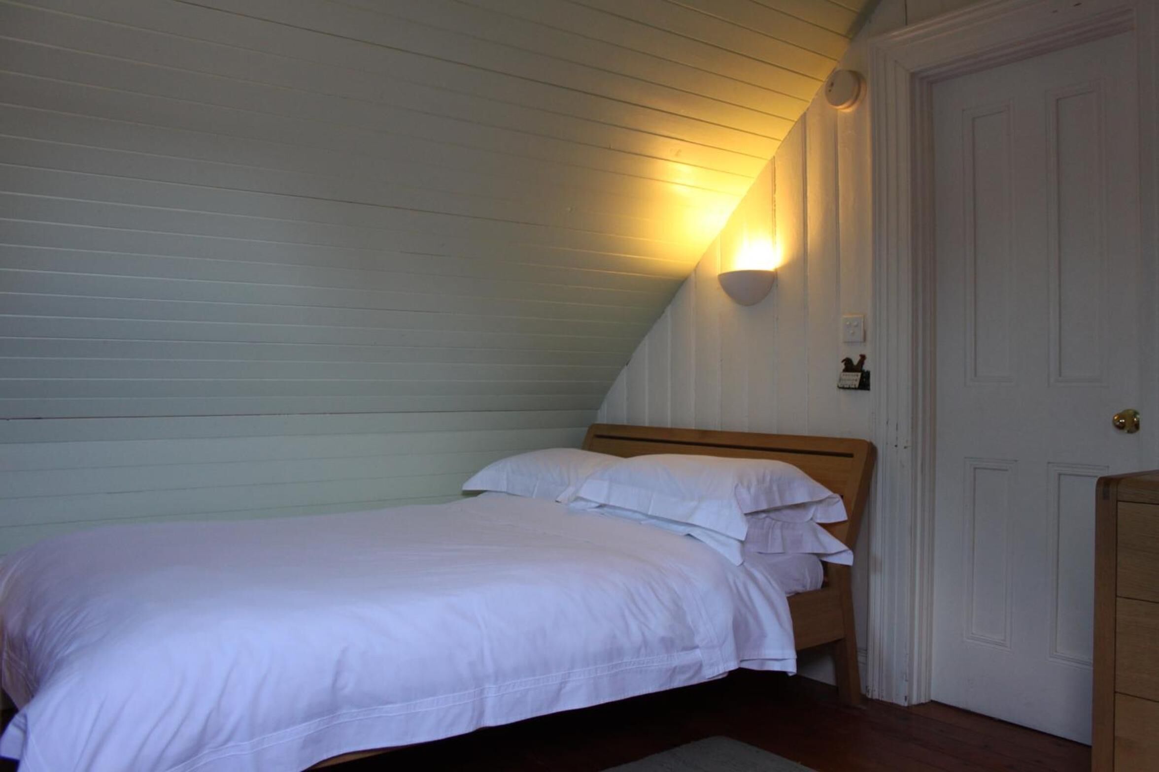 Een slaapkamer met een enkel bed, een houten hoofdbord, een nachtkastje en een wandlamp.