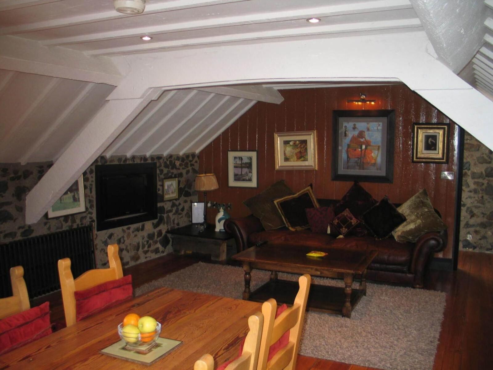 An attic room with a wooden dining table, a sofa, and a TV mounted on the wall.