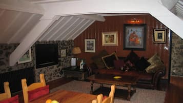 An attic room with a wooden dining table, a sofa, and a TV mounted on the wall.