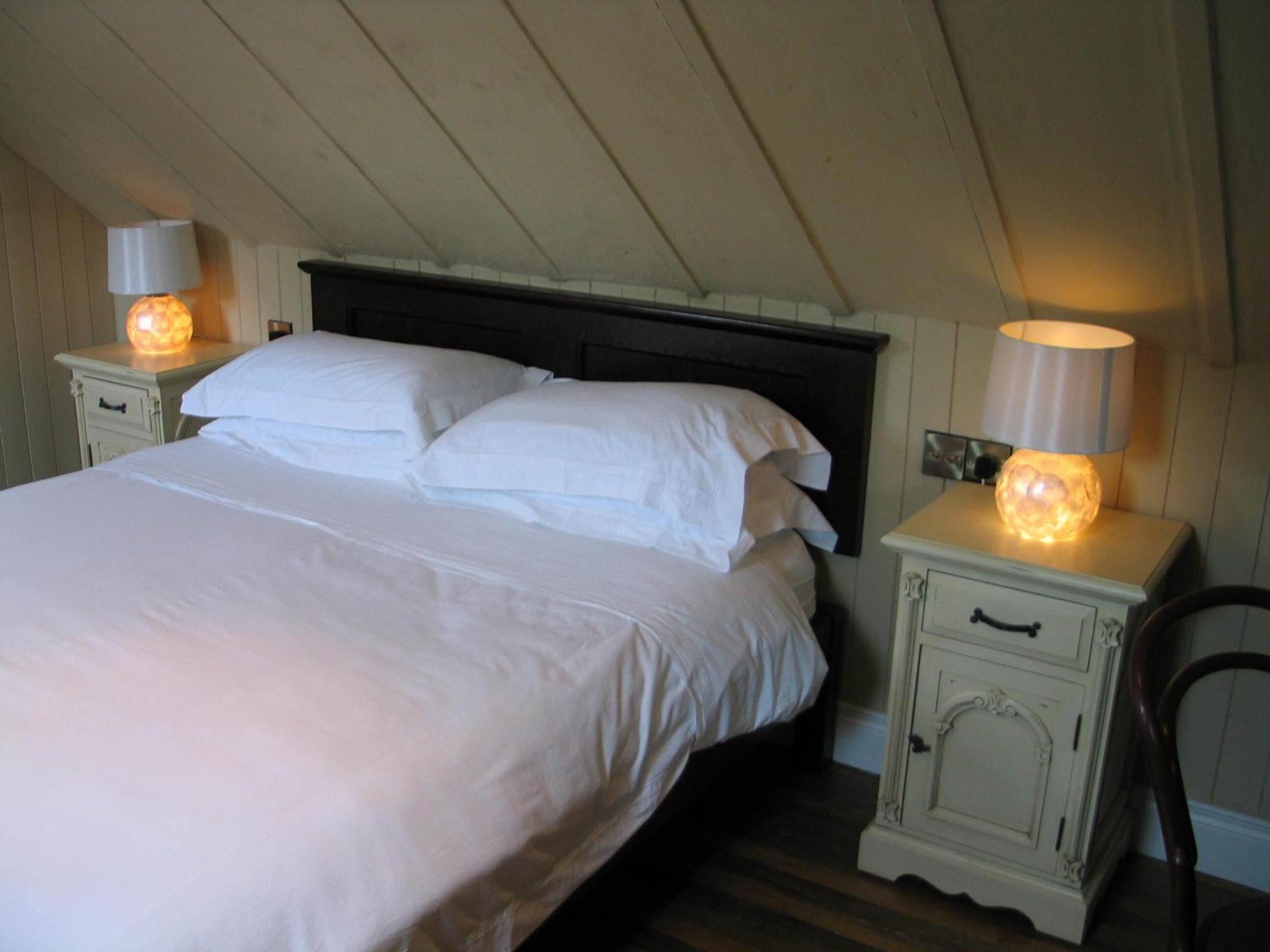 A bedroom with a large bed, two bedside tables with lamps, and a wooden headboard.