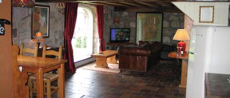 A rustic interior with a stone wall, wooden furniture, a television, and a refrigerator.