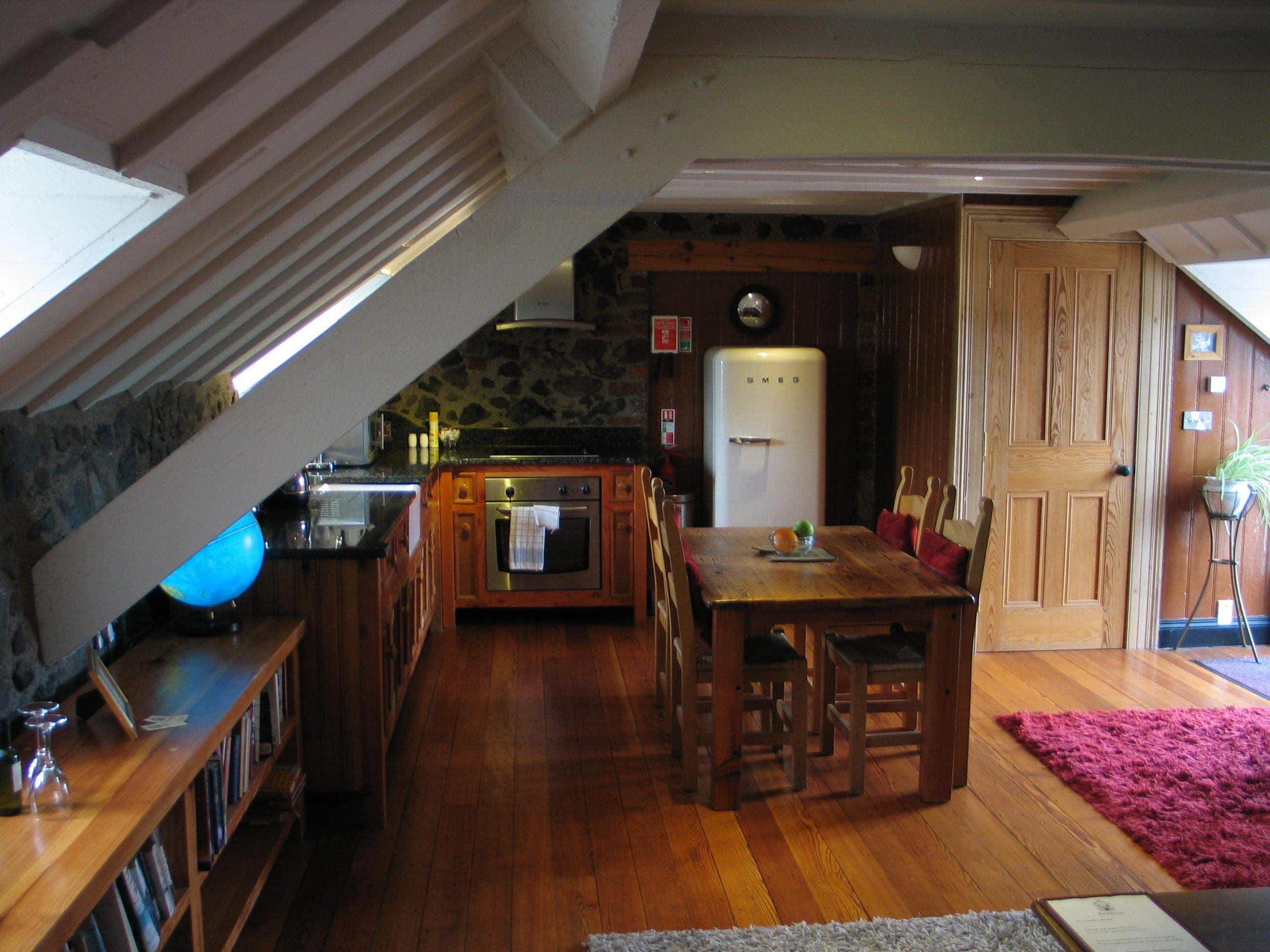 A kitchen with wooden cabinets, a stone wall, a refrigerator, and a dining table with chairs.