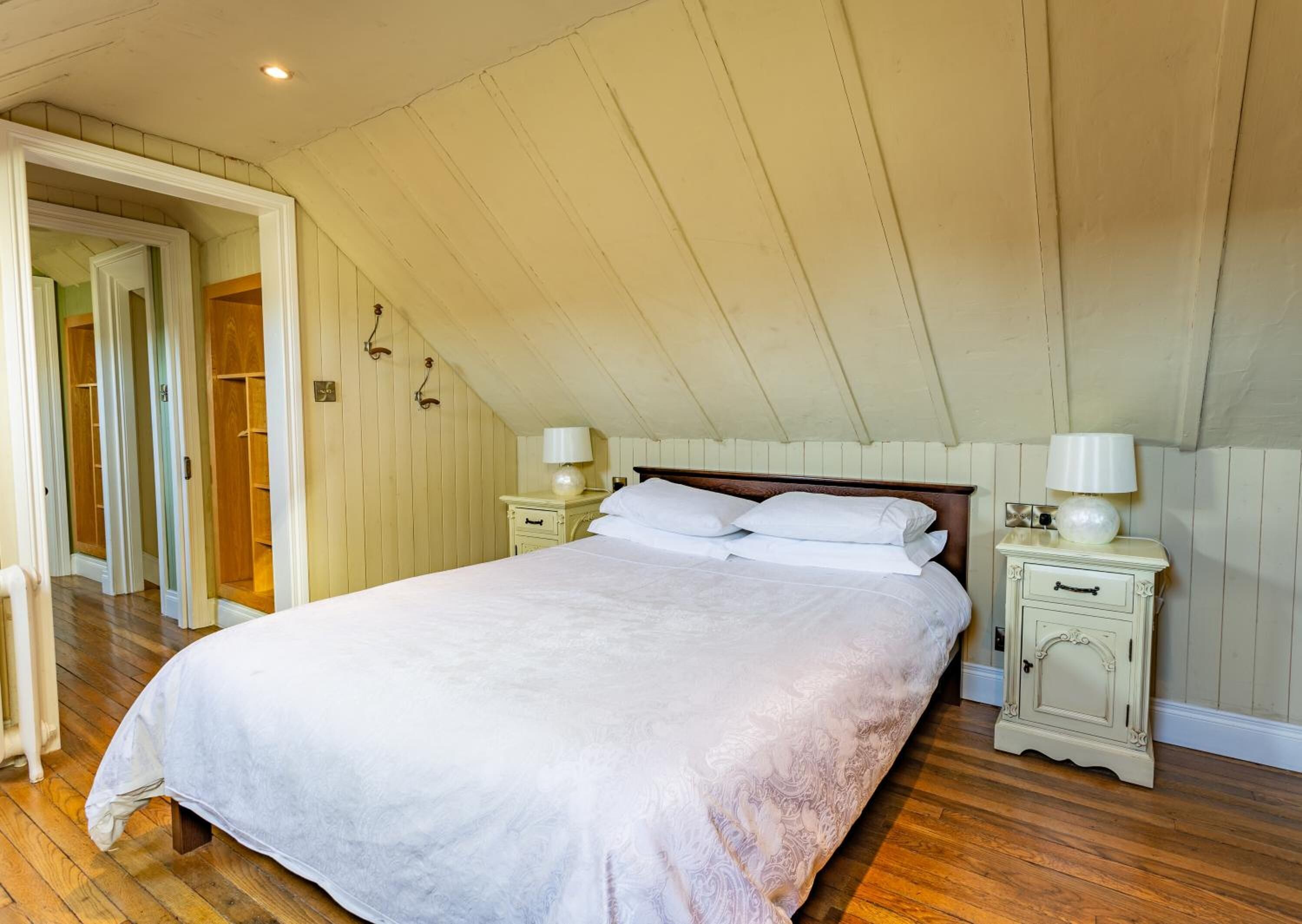A bedroom with a large bed, wooden floors, and a sloped ceiling.