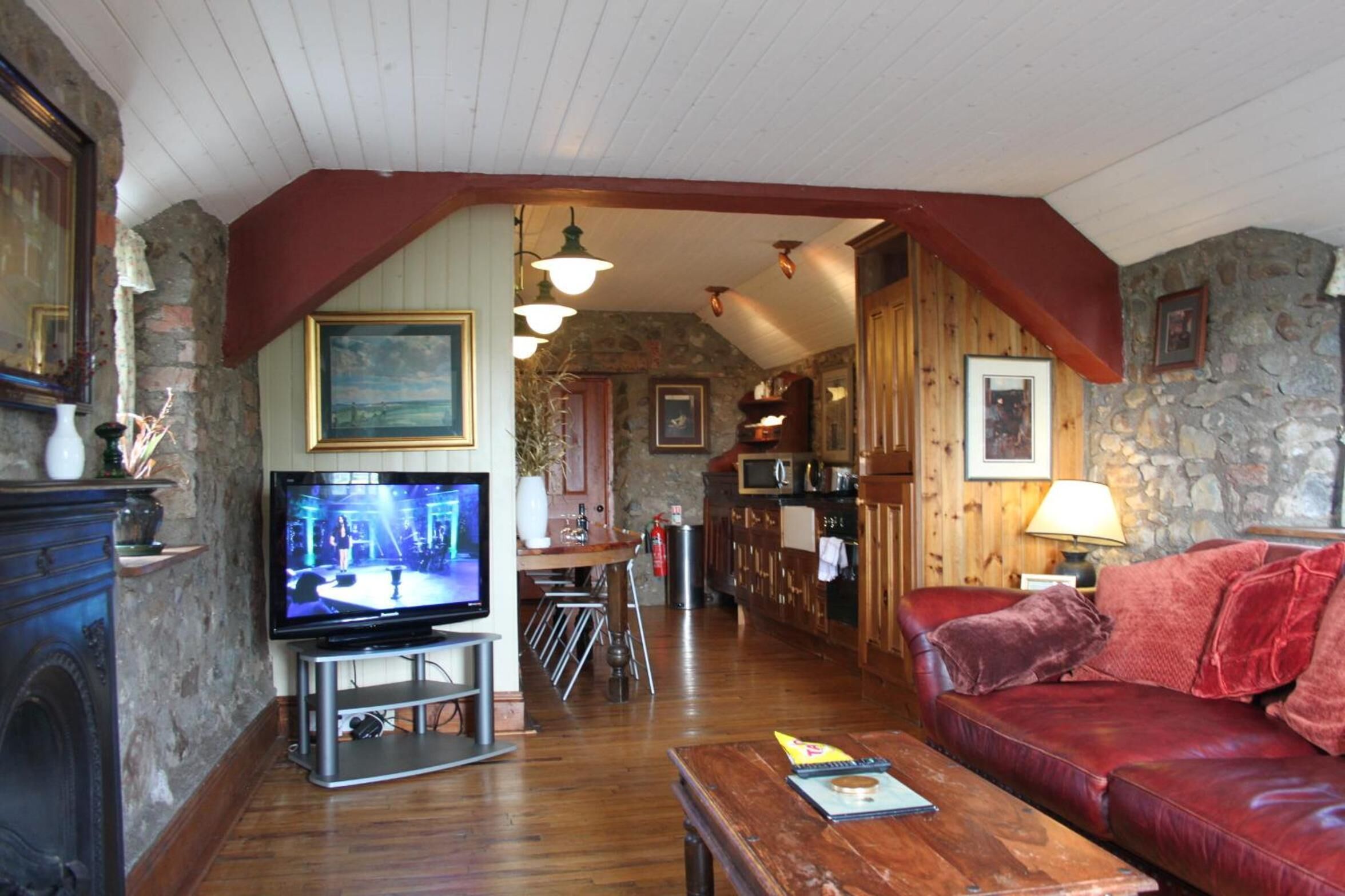 A cozy living room with a television, wooden furniture, stone walls, and a stone fireplace.
