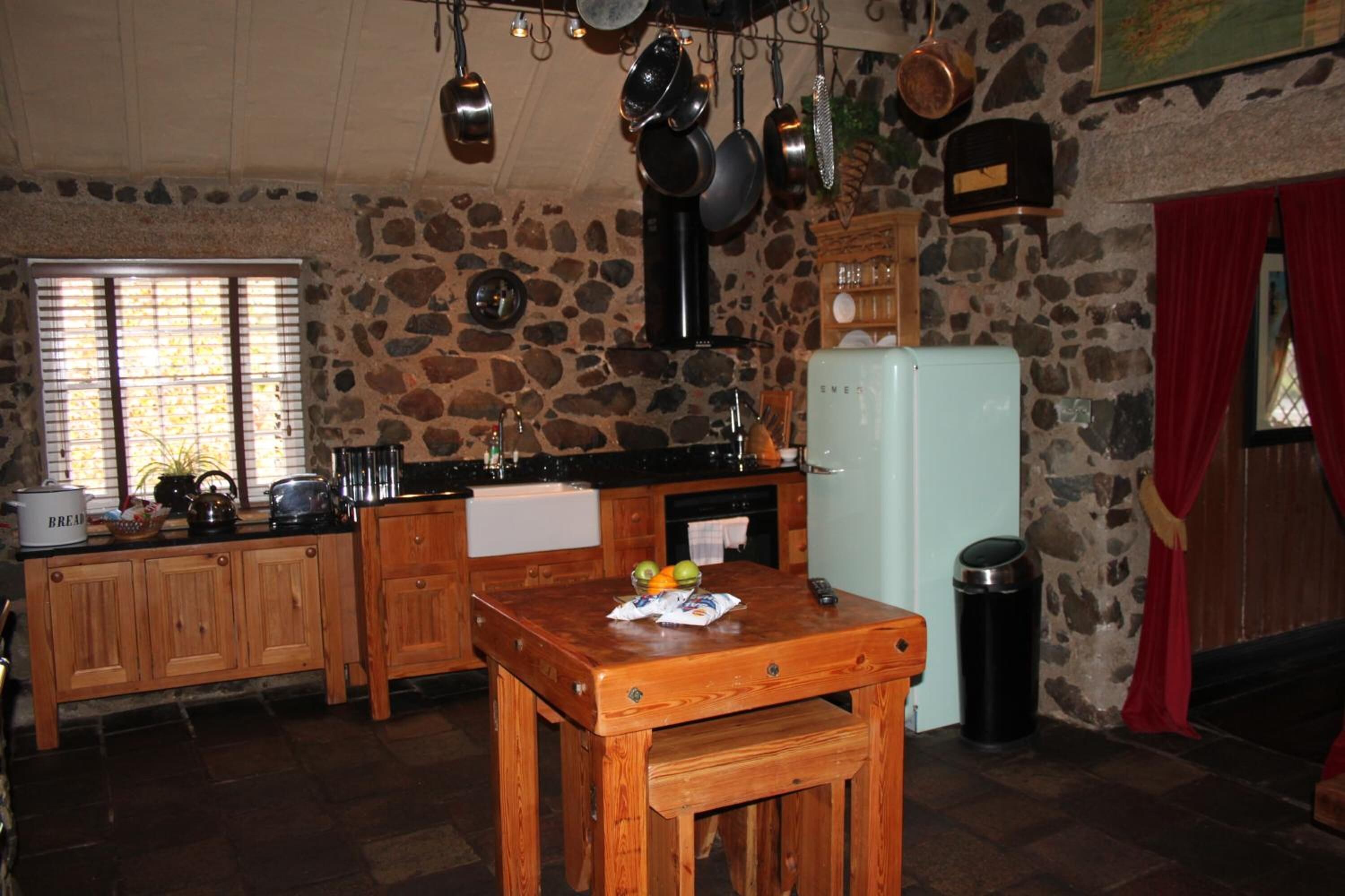 Una cocina rústica con paredes de piedra, armarios de madera y un refrigerador antiguo.