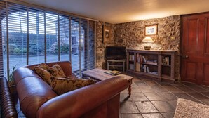 A living room with a leather sofa, a coffee table, a stone fireplace, a television, and a bookshelf. - Clenaghans (Craigavon)