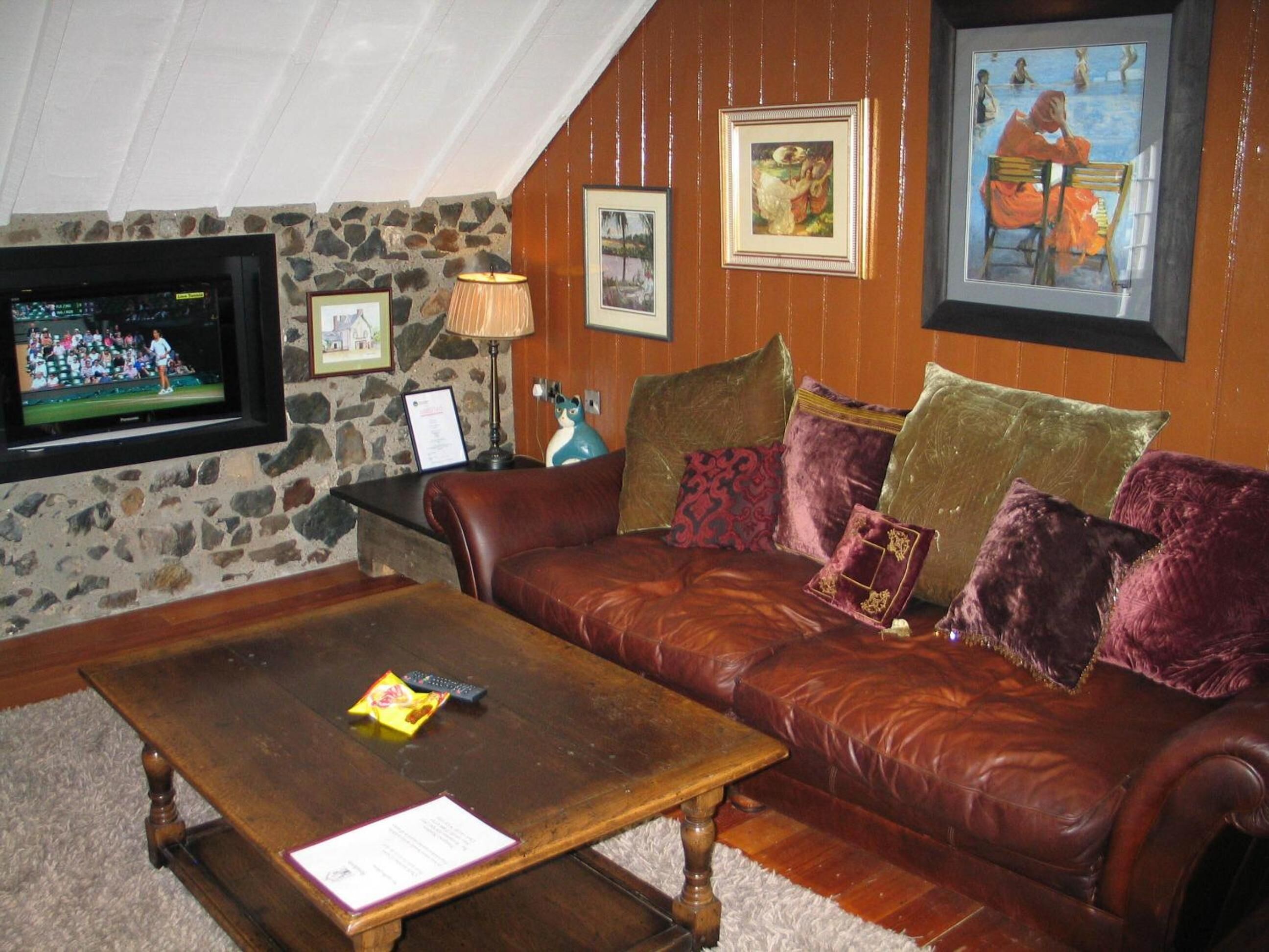 A cozy living room with a leather sofa, a wooden coffee table, and a stone wall.