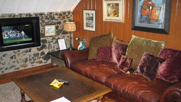 A cozy living room with a leather sofa, a wooden coffee table, and a stone wall.