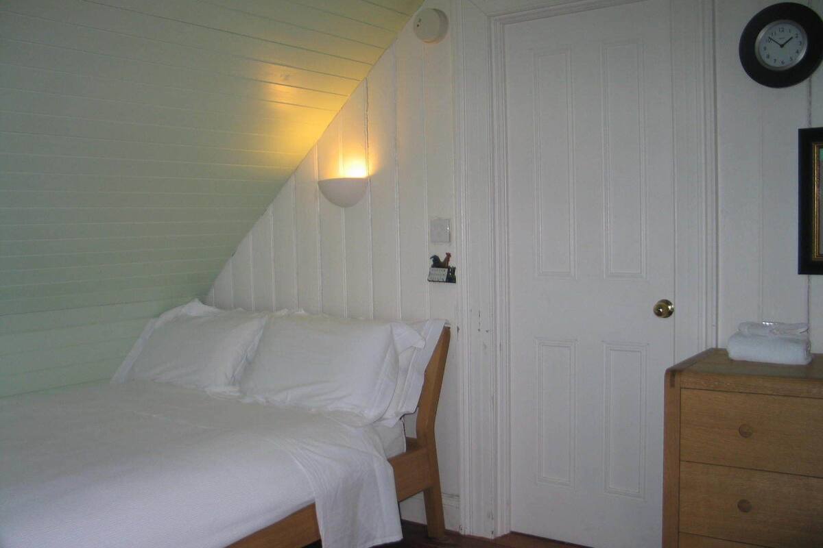 Un dormitorio con una cama individual, un aparador de madera, un reloj en la pared y una puerta con un pequeño estante encima.