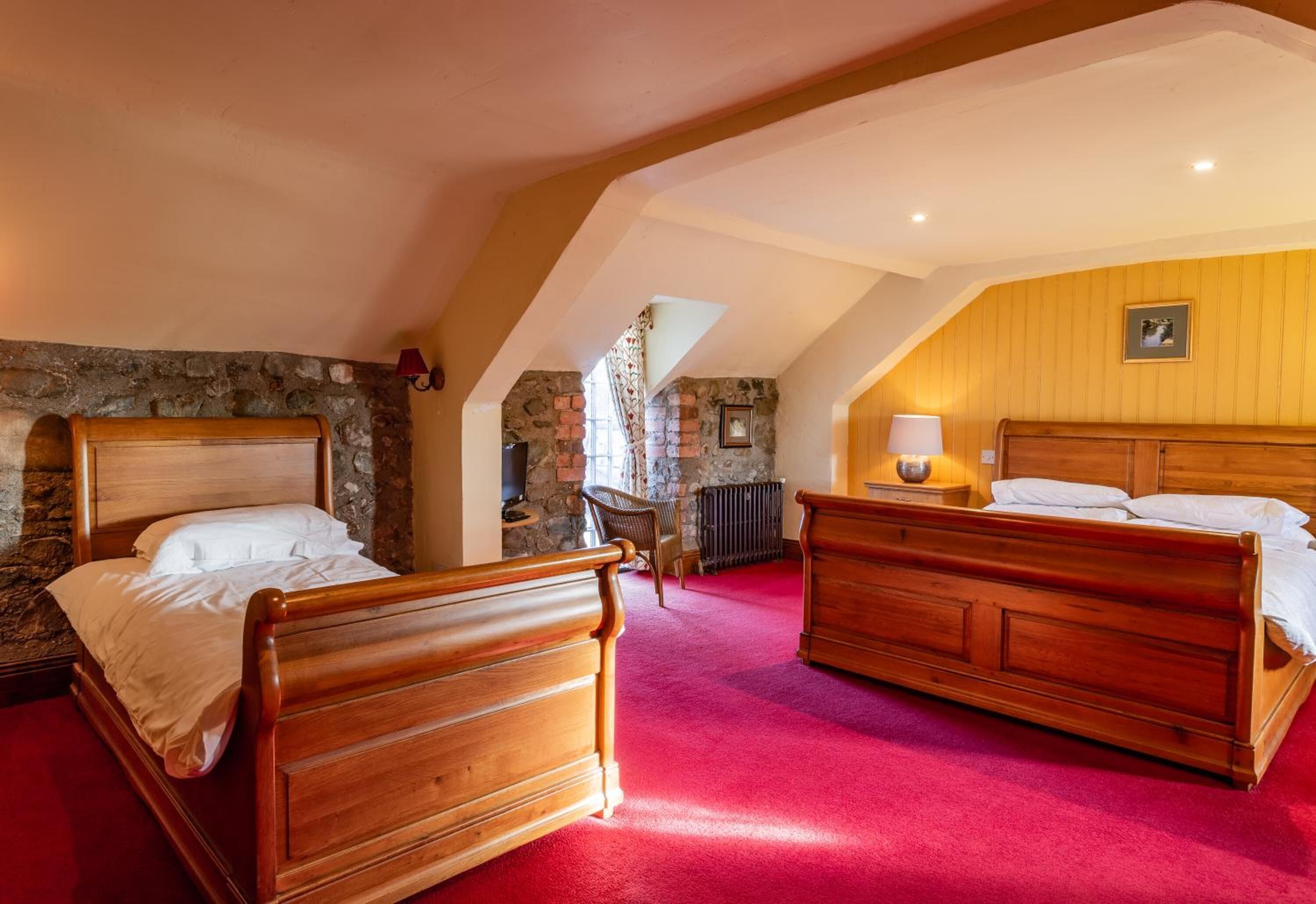 A bedroom with two wooden beds, a stone wall, a red carpet, and a wooden ceiling.