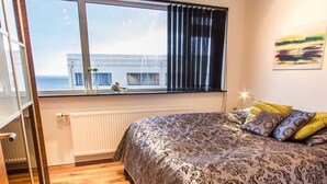 Un dormitorio con una cama grande, una ventana con cortinas, un radiador y vistas a un edificio.