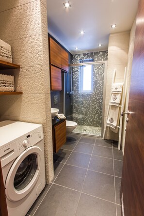 Een moderne badkamer met een wasmachine, toilet, douche en handdoekhouder.