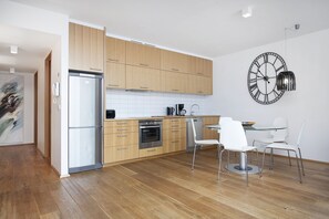 Eine moderne Küche mit Holzausstattung, einem Edelstahlkühlschrank, einer Kaffeemaschine und einer Wanduhr.