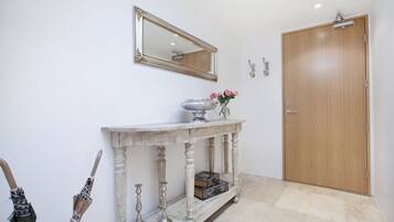 Un couloir avec une porte en bois, un miroir, une console sur laquelle est posé un vase de fleurs et un banc avec un coffre.