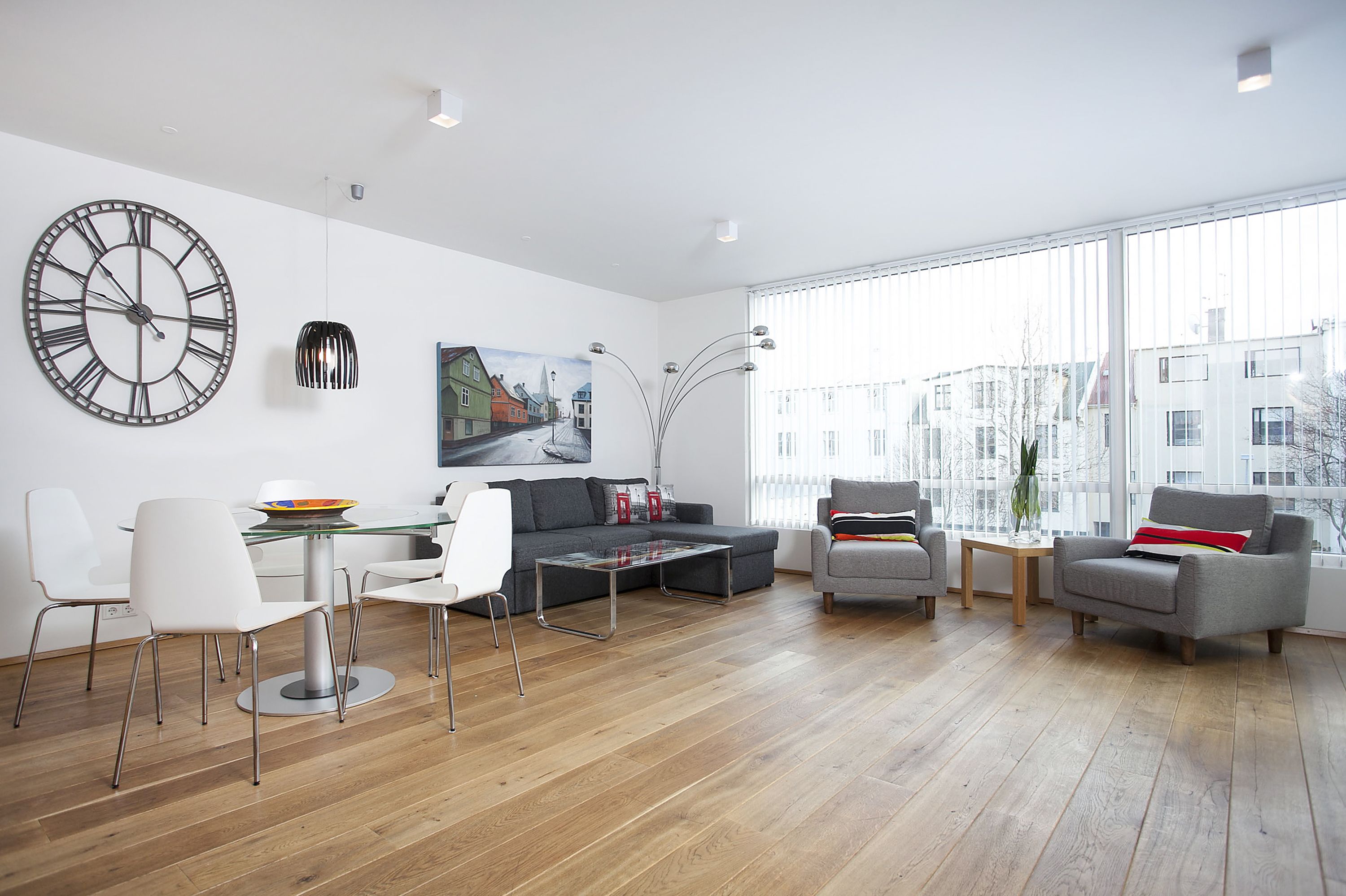 A modern living room with a large wall clock, a glass dining table, and a sofa.