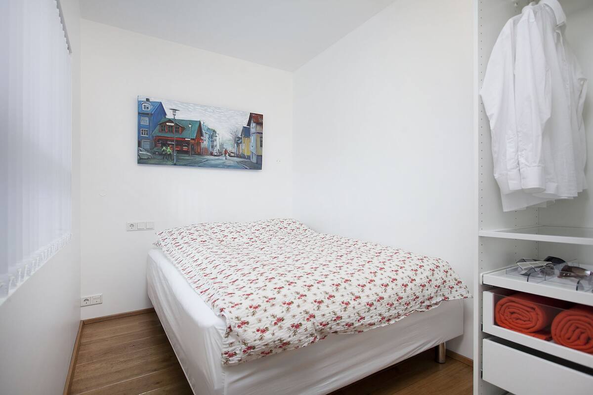 Een slaapkamer met een bed, een schilderij aan de muur, een witte kast en een raam met gordijnen.