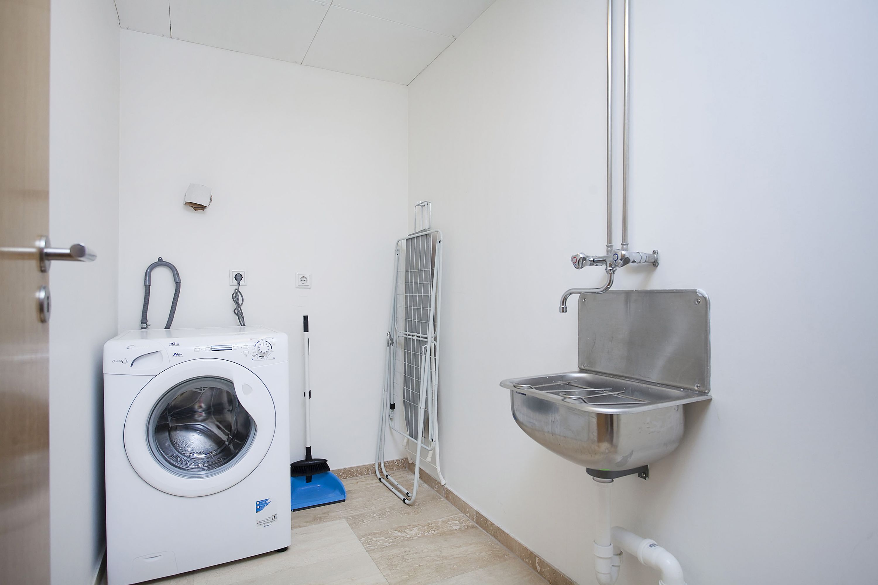 A compact laundry room with a front-loading washing machine, a drying rack, and a sink with a faucet.