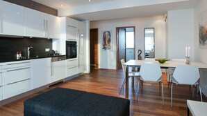 Una cocina moderna con armarios blancos, encimera negra y una zona de comedor con mesa y sillas blancas.