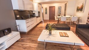 Una cocina moderna con armarios blancos, un comedor con mesa y sillas blancas, y una sala de estar con sofá y mesa de centro.