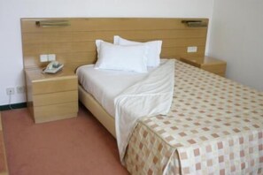 A single bed with a wooden headboard, a bedside table with a phone, and a patterned bedspread.