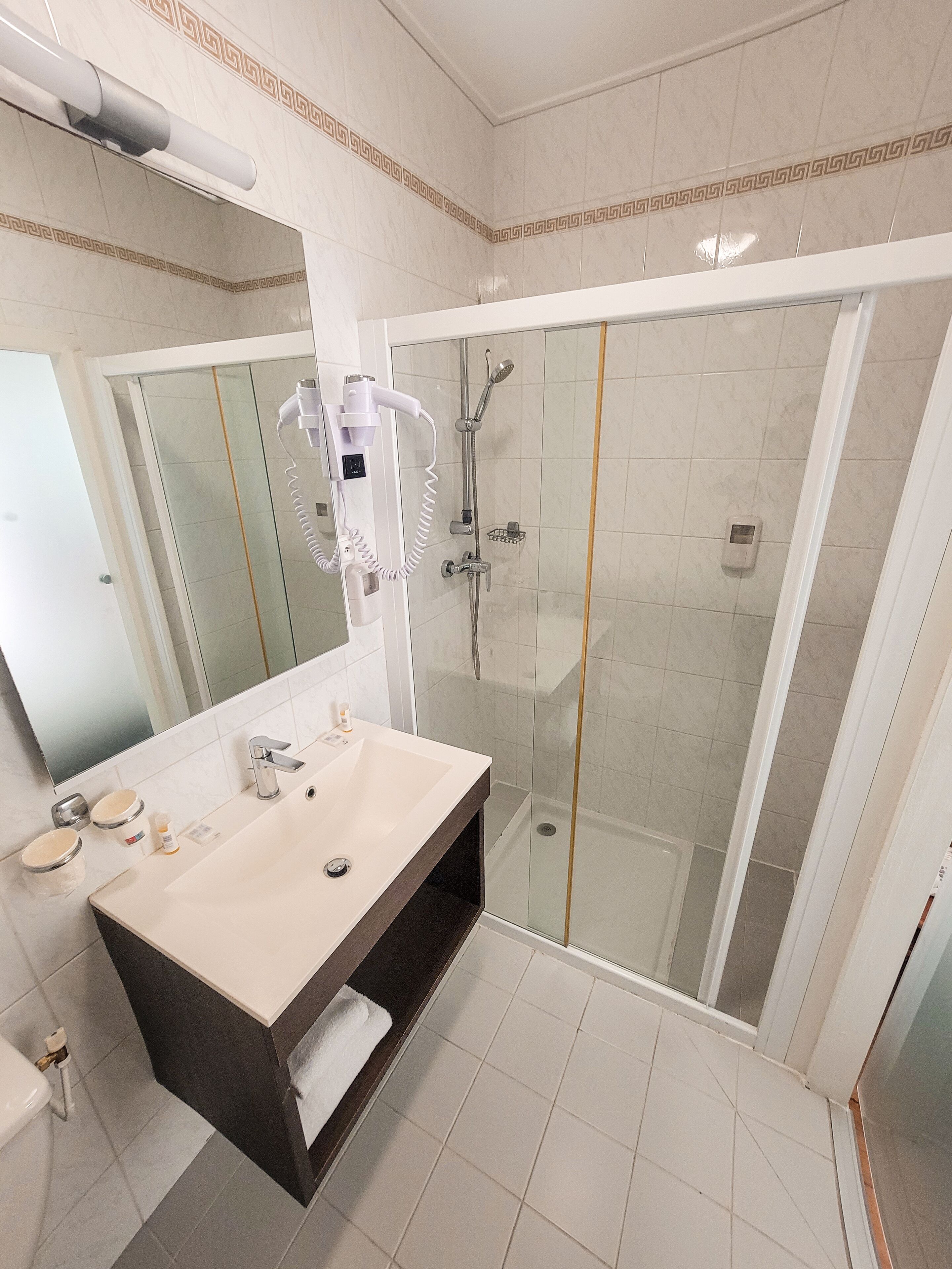 A modern bathroom with a large mirror, a sink with a dark vanity, a shower with a glass door, and a toilet.