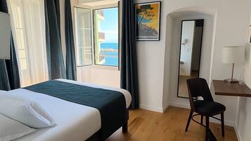 A hotel room with a bed, a desk, a chair, a large window with a view, and a painting on the wall.