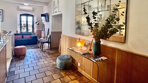A hotel lobby with a blue sofa, a wooden reception desk, a mirror, and a potted plant. - Hôtel Posta Vecchia (Bastia)