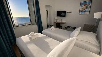 Habitación de hotel con dos camas, un escritorio, una silla, un televisor y vista al mar.
