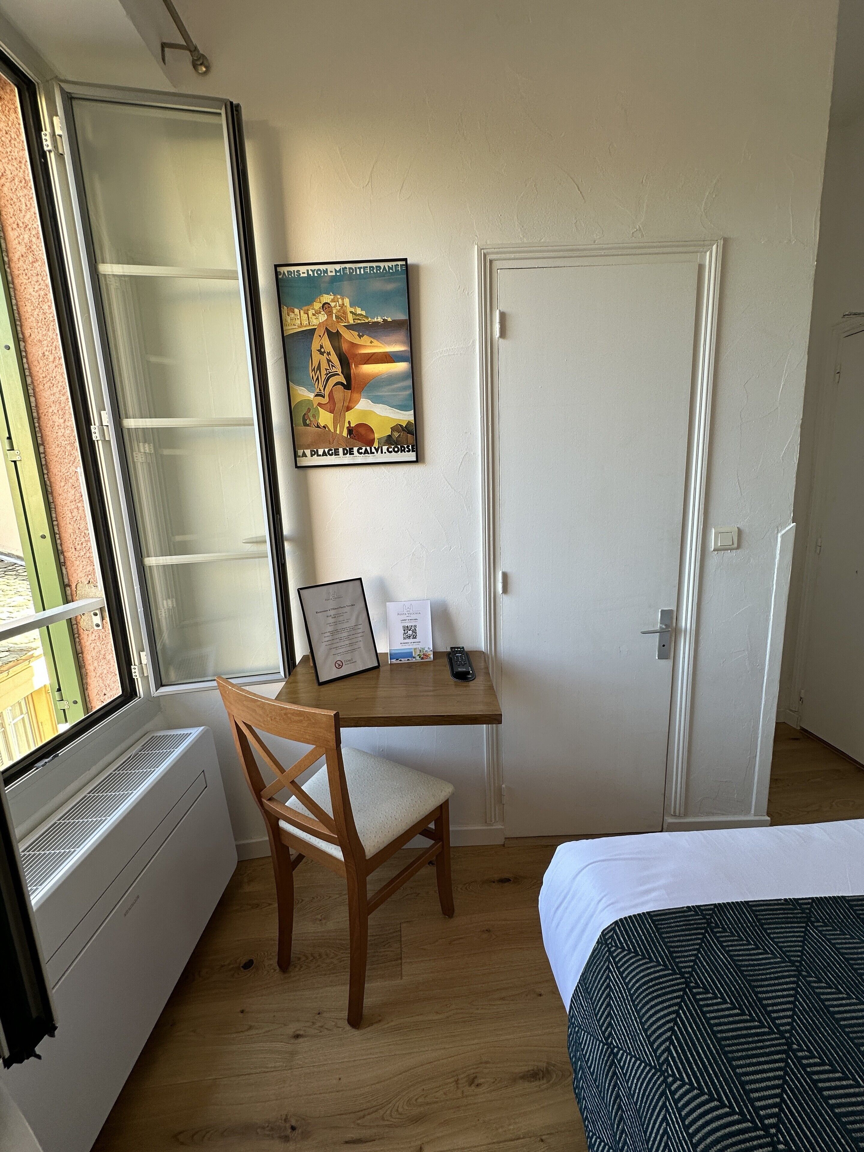 Una habitación con cama, escritorio, silla, radiador, ventana y puerta.