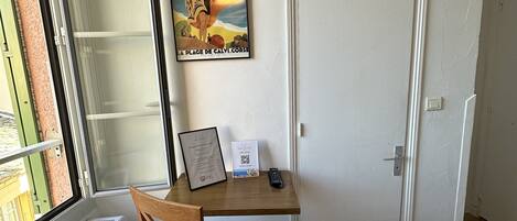 A room with a bed, a desk with a chair, a radiator, a window, and a door.