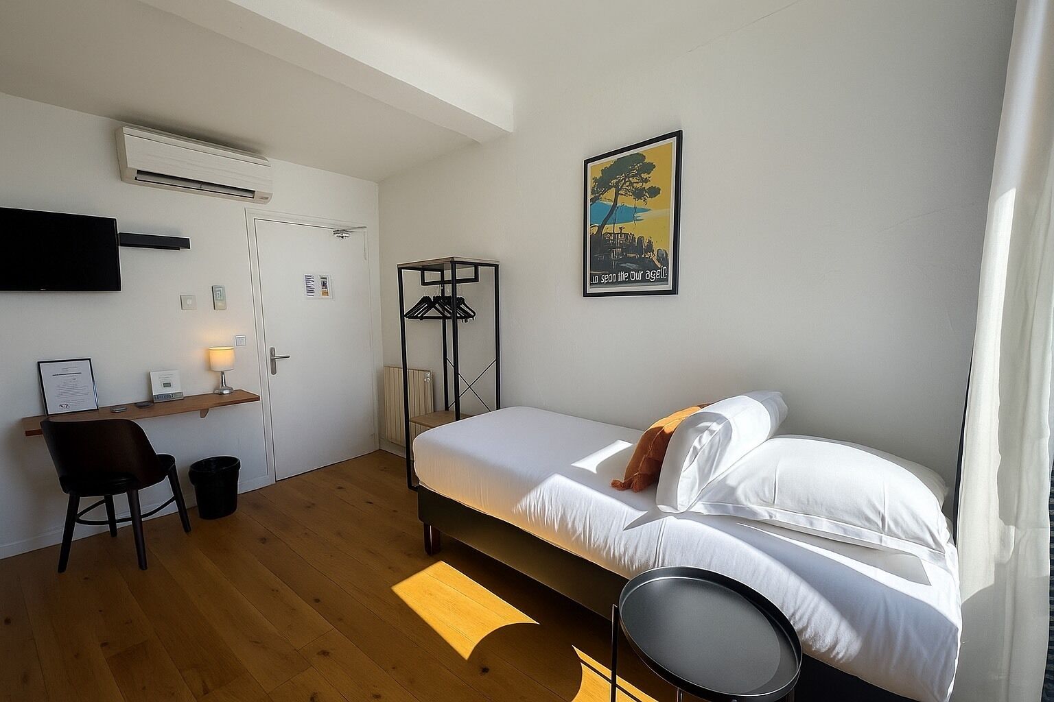 A bedroom with a bed, a desk, a chair, a standing lamp, and a framed picture on the wall.