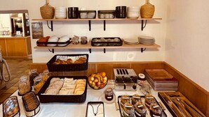 A buffet setup with various food items, including bread, fruits, and condiments, arranged on tables and shelves. - Hôtel Posta Vecchia (Bastia)