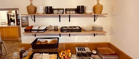 Montaje de bufé con diferentes opciones de comida, como pan, frutas y salsas, dispuestas sobre mesas y estantes.