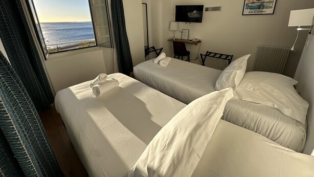 A hotel room with two beds, a desk, a chair, a lamp, and a poster on the wall. - Hôtel Posta Vecchia (Bastia)