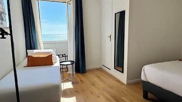 Une chambre avec deux lits, une petite table, une chaise, une fenêtre avec des rideaux et une vue sur la mer.