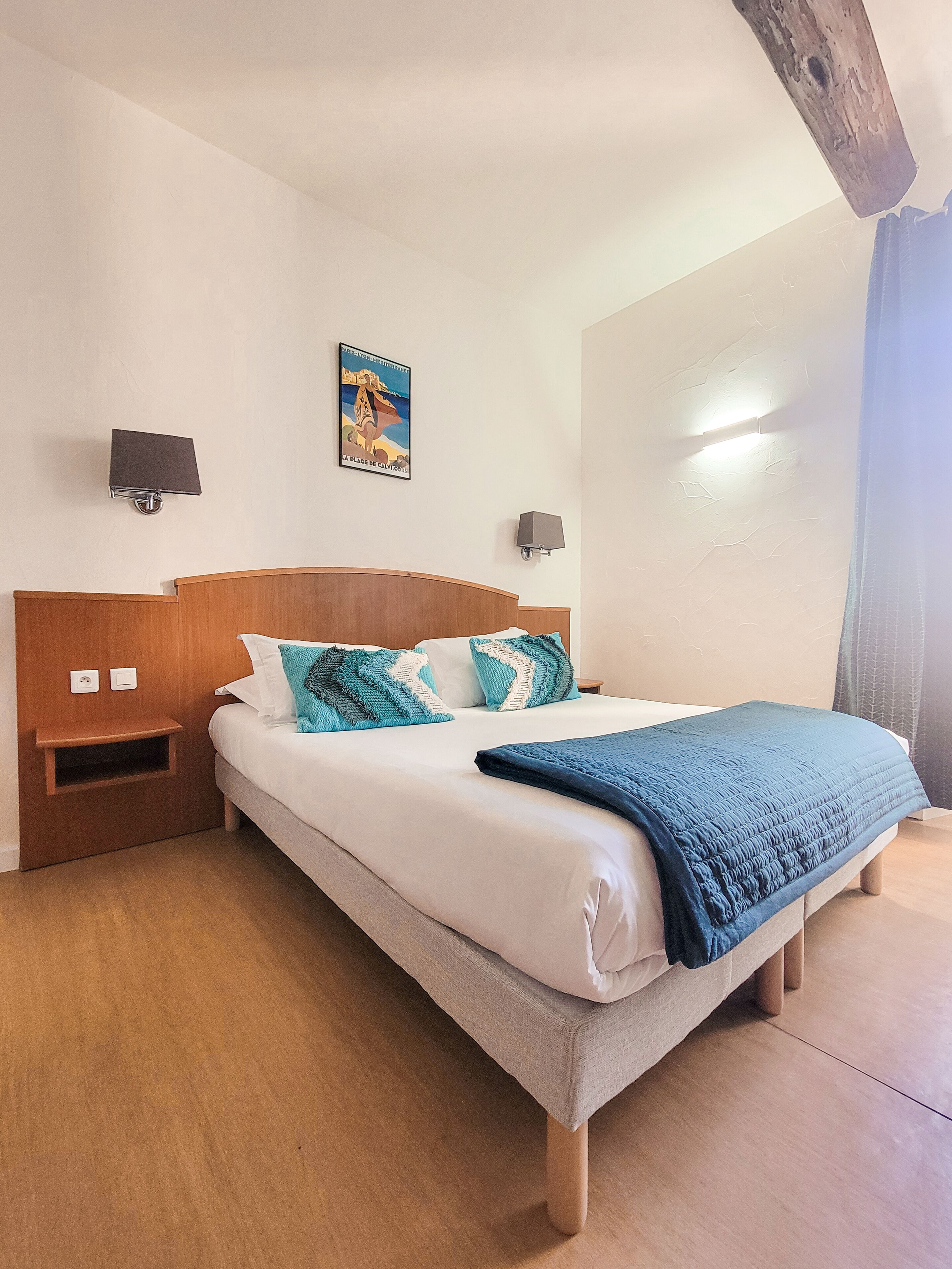 A neatly made bed with a blue blanket, wooden headboard, and two wall-mounted lamps.
