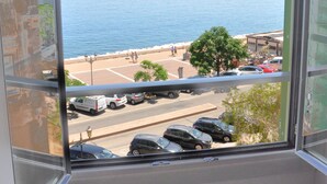 A balcony with a view of the sea, parked cars, and a building with stone walls. - Hôtel Posta Vecchia (Bastia)
