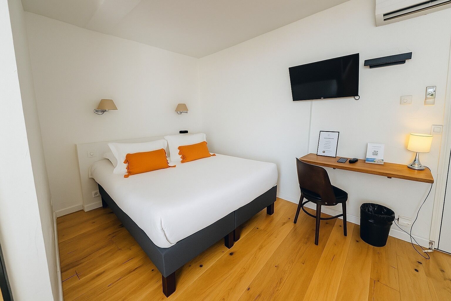 Une chambre d’hôtel équipée d’un lit, d’un bureau, d’une chaise, d’une télévision et d’une poubelle.