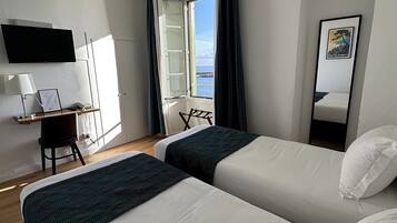 A hotel room with two beds, a desk with a chair, a TV, and a window with curtains.