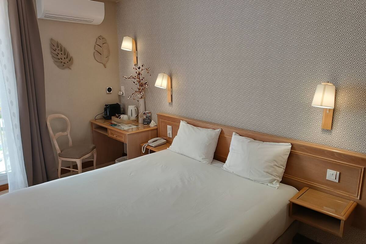 Une chambre d’hôtel avec un grand lit, un bureau avec une chaise, une table de chevet et une lampe fixée au mur.