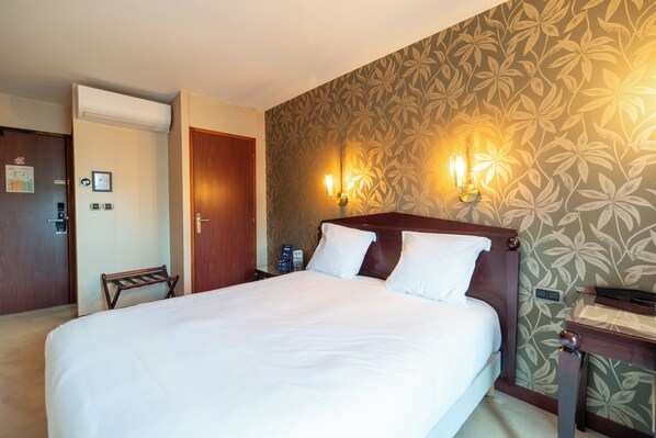 Una habitación de hotel con una cama grande, un cabecero de madera, dos lámparas de pared, un banco de madera y una puerta.