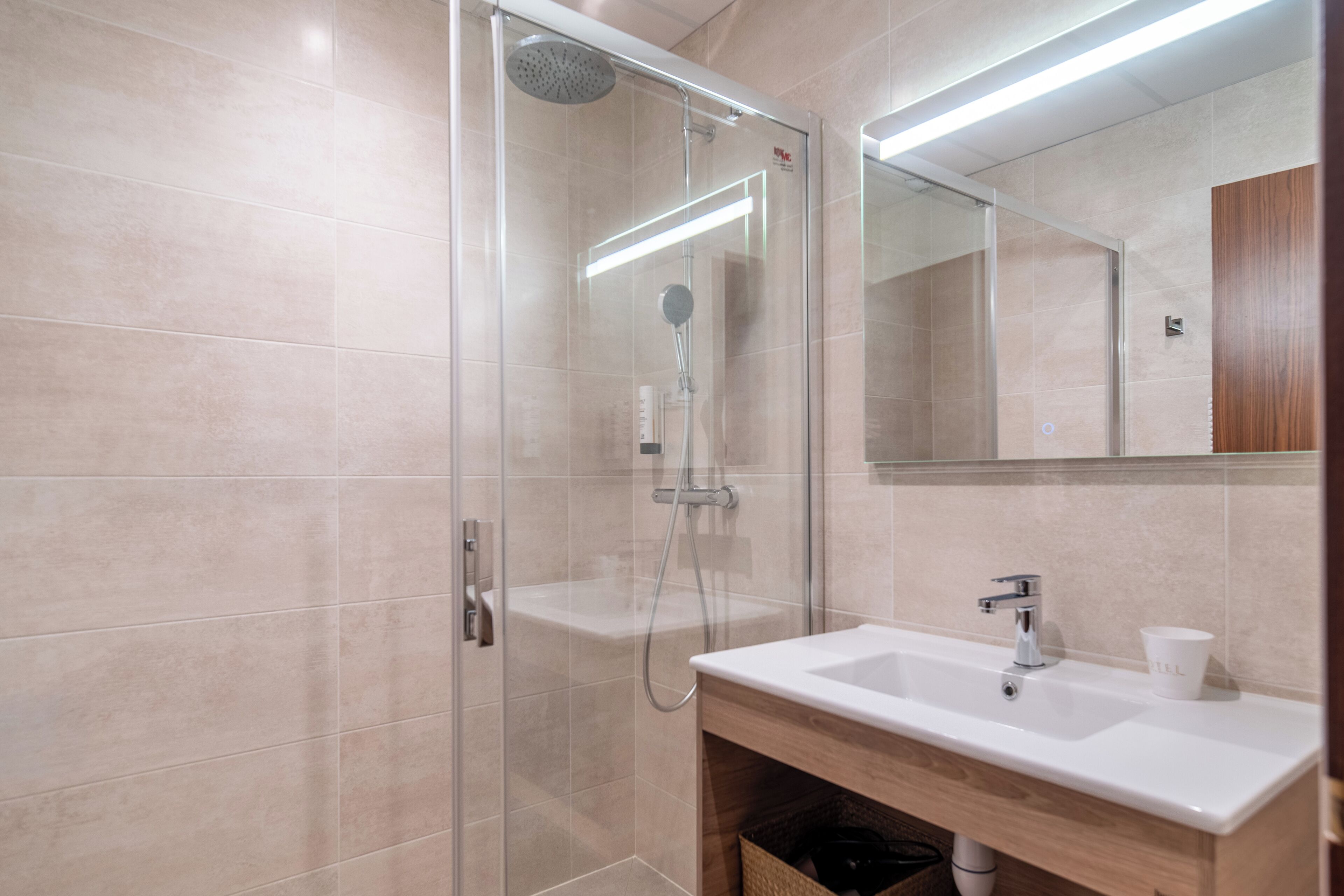 Un baño moderno con ducha de vidrio, un lavabo blanco y un espejo sobre él.
