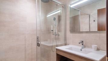 Un baño moderno con ducha de vidrio, un lavabo blanco y un espejo sobre él.