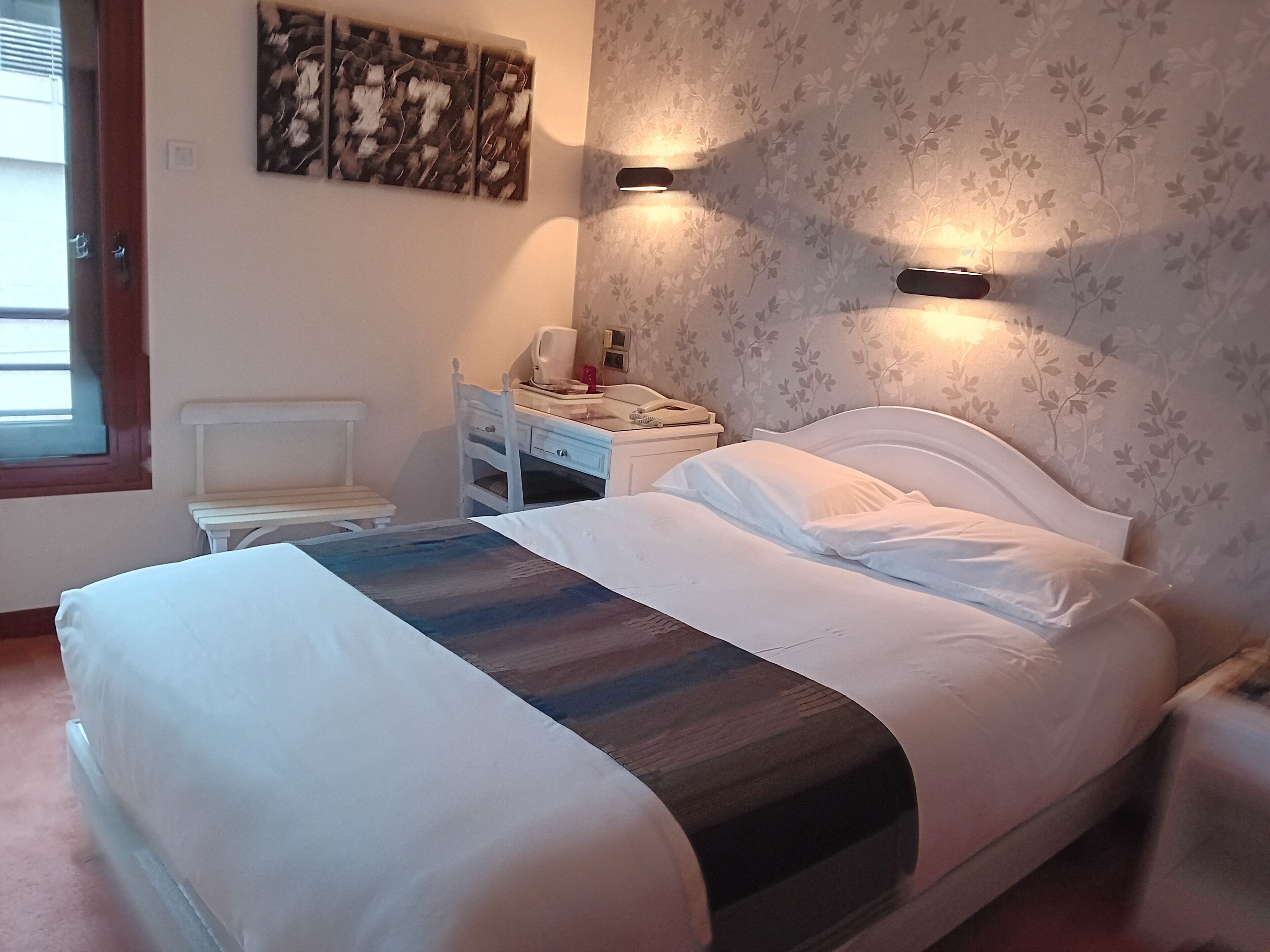 Une chambre à coucher comprenant un lit, une table de chevet, une chaise et une œuvre d’art accrochée au mur.
